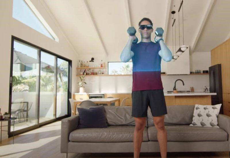 A guy working out with dumbbells in his living room, wearing VR Goggles.